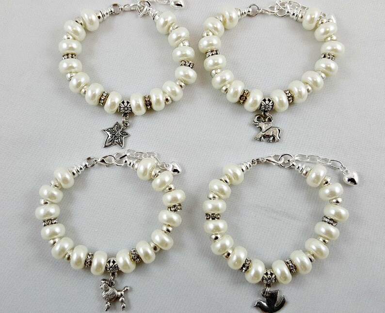 May include: Four white pearl bracelets with silver charms. The charms are a star, a deer, a bird, and a rooster.