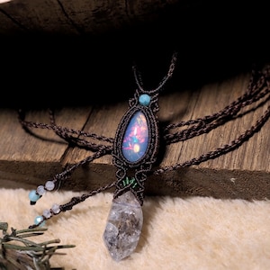 May include: A handmade macramé necklace with a teardrop-shaped iridescent stone pendant, a small turquoise bead, and a clear quartz crystal. The necklace is made with brown cord and has a bohemian style.