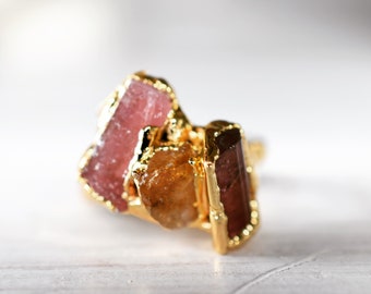 Può includere: Un anello d'oro con tre pietre grezze: una rosa, una marrone e una gialla. Le pietre sono incastonate in una fascia d'oro.