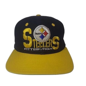 Puede incluir: Una gorra de béisbol negra con visera amarilla. La parte frontal presenta el texto bordado Steelers en letras grandes amarillas, con el emblema del logo de los Pittsburgh Steelers centrado sobre la palabra y la palabra Pittsburgh impresa en blanco.