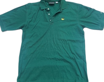 Puede incluir: Un polo de manga corta de color verde oscuro con cuello, tapeta de tres botones y un pequeño logotipo bordado en el pecho izquierdo que representa un mapa amarillo de los Estados Unidos con un alfiler rojo.