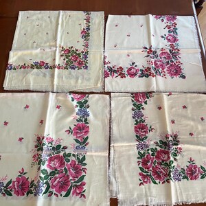 May include: Four white cotton handkerchiefs with a floral pattern in shades of pink, green, and purple. The handkerchiefs have a scalloped edge.