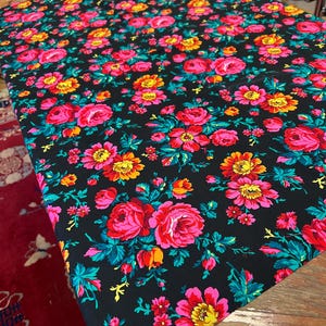 May include: Black fabric with a floral pattern featuring pink, yellow, and red roses on a black background. The fabric has a repeating pattern of flowers and leaves.