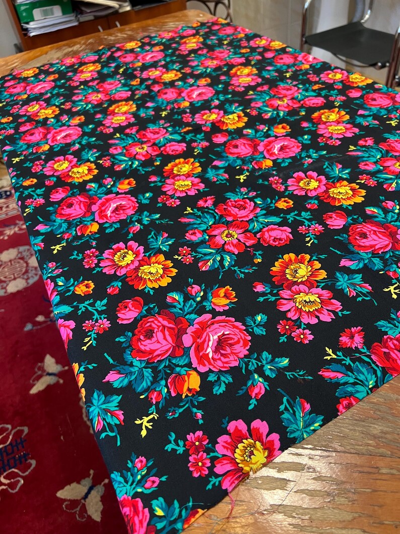 May include: Black fabric with a floral pattern featuring pink, yellow, and red roses on a black background. The fabric has a repeating pattern of flowers and leaves.