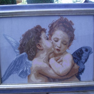 Könnte beinhalten: Ein gerahmtes Nadelbild, das zwei sich umarmende und küssende Cherubim darstellt. Die Cherubim haben braunes Haar und sind mit Flügeln dargestellt. Der Hintergrund ist hellblau.