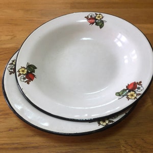 May include: Two white enamel bowls with black rims and floral designs. The bowls feature red roses, white flowers, and green leaves.