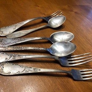 May include: A set of five vintage silverware pieces, including three spoons and two forks, with ornate designs and a silver finish.