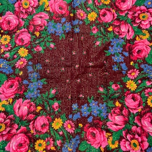Puede incluir: Textil burdeos con estampado floral. El diseño presenta grandes rosas rosas, flores azules y amarillas y hojas verdes. El fondo tiene un sutil efecto brillante.