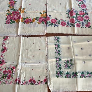 May include: Four white cotton handkerchiefs with floral patterns. The handkerchiefs have pink, purple, and green floral designs on a white background. The handkerchiefs are all the same size and have a fringed edge.