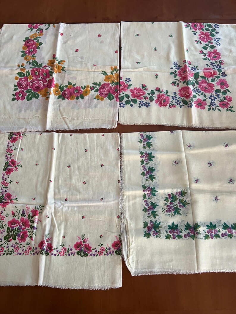 May include: Four white cotton handkerchiefs with floral patterns. The handkerchiefs have pink, purple, and green floral designs on a white background. The handkerchiefs are all the same size and have a fringed edge.