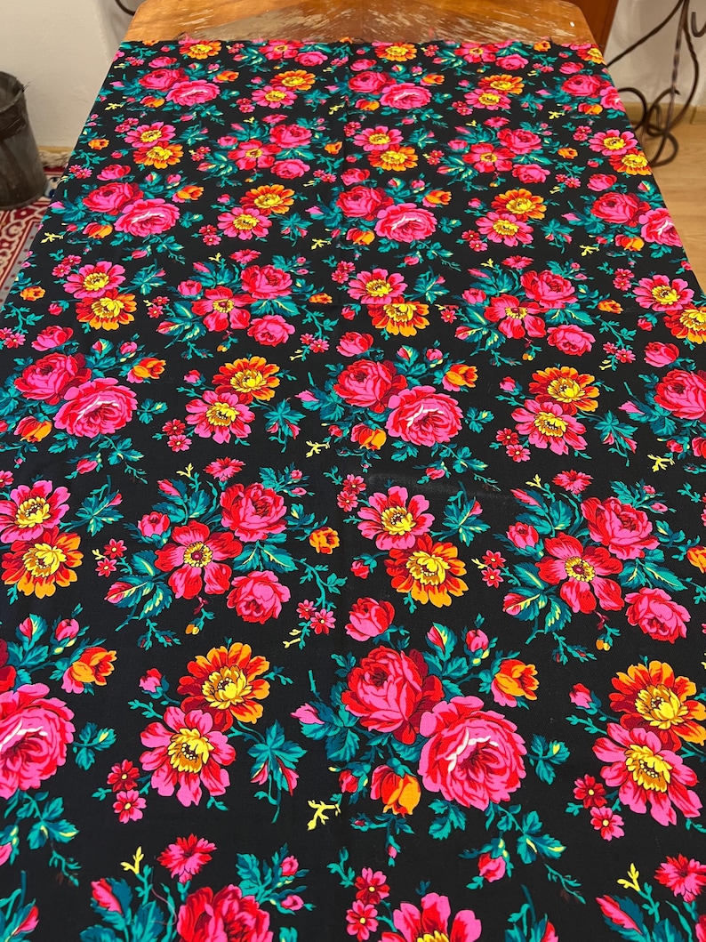 May include: Black fabric with a repeating pattern of pink, red, yellow, and green flowers. The flowers are stylized and have a vintage look.