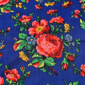 Puede incluir: Primer plano de una tela azul adornada con un diseño floral. El patrón presenta grandes rosas rojas, flores más pequeñas rosas, amarillas y azules, y follaje verde. El diseño es detallado y colorido, creando una apariencia rica y texturizada.