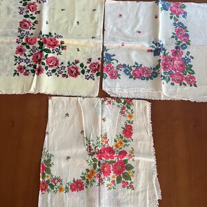 May include: Three white cotton handkerchiefs with floral patterns. The handkerchiefs have pink, yellow, blue, and green flowers. The handkerchiefs have a frayed edge.