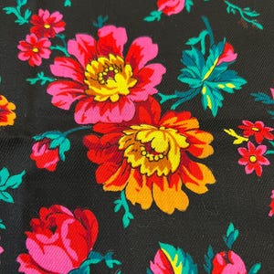 May include: Black fabric with a floral pattern featuring pink, red, yellow, and green flowers. The flowers are stylized and have a vintage look.