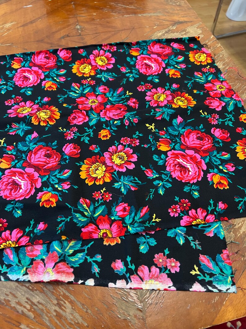 May include: Two pieces of black fabric with a floral pattern. The fabric features pink, red, yellow, and green flowers on a black background.