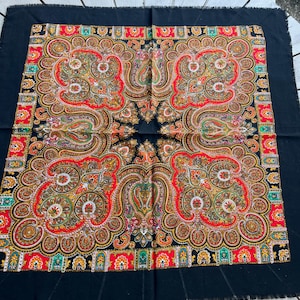 Puede incluir: Un pañuelo cuadrado negro con un vibrante patrón de cachemira simétrico en tonos rojo, naranja, amarillo, verde y blanco. La tela tiene un borde deshilachado y muestra intrincados motivos florales y de lágrima en toda la superficie.