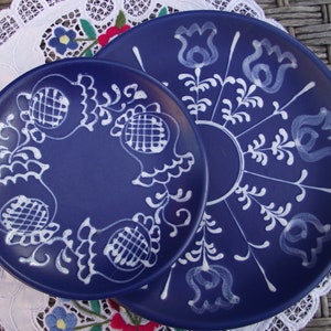 Op de afbeelding: Twee blauwe keramische borden met witte bloemenmotieven. Het kleinere bord ligt op het grotere bord.