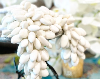 May include: White almond-shaped candies arranged in a cascading display on a black metal stand. The candies are clustered together, creating a visually appealing and festive presentation.
