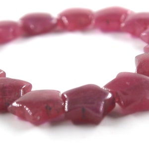 May include: A pink star-shaped gemstone bracelet. The bracelet is made of many small, faceted gemstones that are strung together on a clear elastic cord.