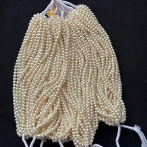 Puede incluir: Un mont&oacute;n de hebras de perlas blancas, atadas con un cordel blanco. Las perlas son peque&ntilde;as y redondas, y est&aacute;n dispuestas en forma de abanico.