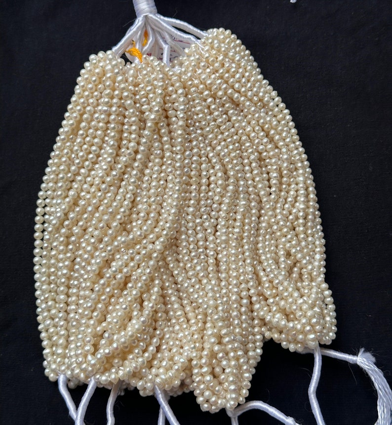 Puede incluir: Un mont&oacute;n de hebras de perlas blancas, atadas con un cordel blanco. Las perlas son peque&ntilde;as y redondas, y est&aacute;n dispuestas en forma de abanico.