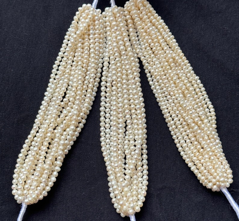 Puede incluir: Una hebra de perlas de agua dulce blancas, con m&uacute;ltiples hebras de perlas agrupadas. Las perlas son peque&ntilde;as y redondas, y la hebra es larga.