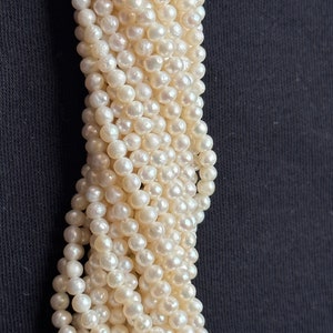 Puede incluir: Una hebra de cuentas de perlas blancas, dispuestas en una espiral suelta, sobre un fondo negro.