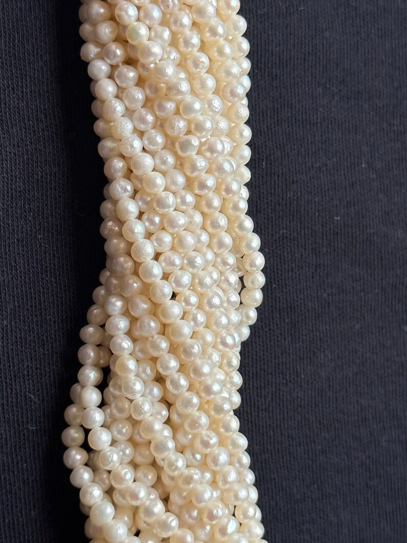 Puede incluir: Una hebra de cuentas de perlas blancas, dispuestas en una espiral suelta, sobre un fondo negro.