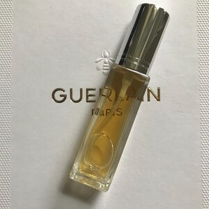 May include: A small, clear glass bottle of perfume with a silver cap. The bottle is filled with a light yellow liquid. The bottle is labelled "Guerlain Paris".
