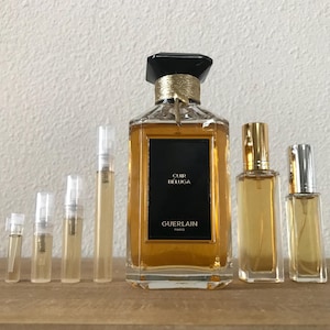May include: A set of perfume bottles, including a large bottle of Guerlain Cuir Beluga perfume and several smaller sample bottles. The bottles are all clear glass with gold accents and the larger bottle has a black cap.