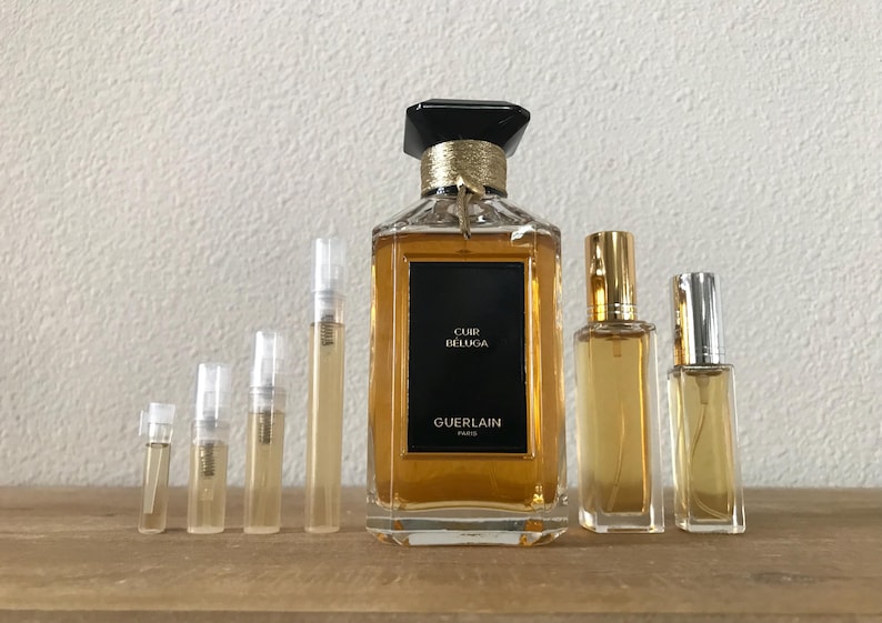 May include: A set of perfume bottles, including a large bottle of Guerlain Cuir Beluga perfume and several smaller sample bottles. The bottles are all clear glass with gold accents and the larger bottle has a black cap.