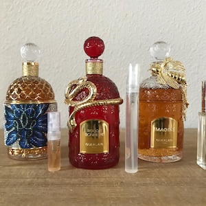 May include: Four bottles of perfume, two with gold caps and two with clear caps. The bottles are all different shapes and sizes. The bottles are on a wooden surface. The bottles are labeled "Rouge  Bonheur" and "Imagine" by Guerlain.