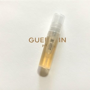 May include: A clear glass bottle containing a gold liquid. The bottle has a white cap and is labelled "Guerlain Paris".