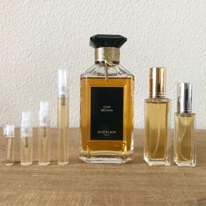 May include: A set of perfume bottles, including a large bottle of Guerlain Cuir Beluga perfume and several smaller sample bottles. The bottles are all clear glass with gold accents and contain a golden liquid.