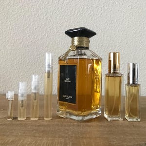 May include: A set of perfume samples in various sizes, including a full-sized bottle of Guerlain Cuir Beluga perfume. The bottles are clear glass with gold accents and a black cap. The full-sized bottle has a label that reads "Cuir Beluga" and "Guerlain Paris".