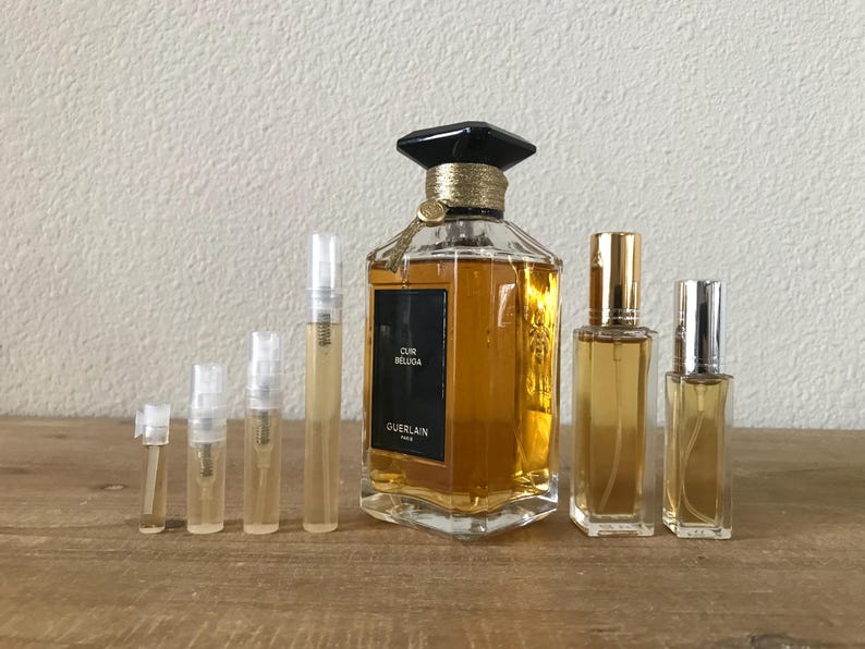 May include: A set of perfume samples in various sizes, including a full-sized bottle of Guerlain Cuir Beluga perfume. The bottles are clear glass with gold accents and a black cap. The full-sized bottle has a label that reads "Cuir Beluga" and "Guerlain Paris".