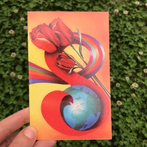 May include: A vintage postcard with a colorful illustration of a globe surrounded by a rainbow and three red tulips.
