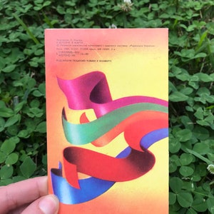 May include: A vintage postcard featuring an abstract design of colorful ribbons in red, blue, green, and yellow. The postcard is from 1985 and features the text "В БЕРЕЗНЯ. В МАРТА." and "ВІДСИЛАТИ ПОШТОЮ ТІЛЬКИ У КОНВЕР&Tau;&Iota;".
