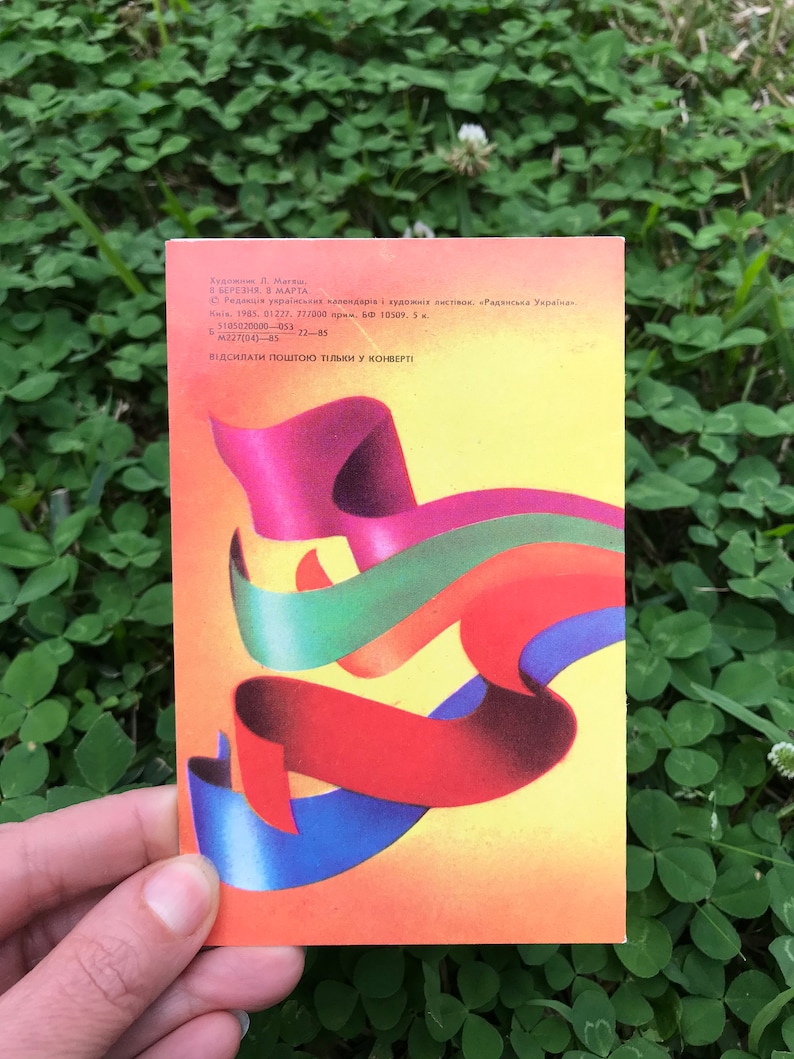 May include: A vintage postcard featuring an abstract design of colorful ribbons in red, blue, green, and yellow. The postcard is from 1985 and features the text "В БЕРЕЗНЯ. В МАРТА." and "ВІДСИЛАТИ ПОШТОЮ ТІЛЬКИ У КОНВЕР&Tau;&Iota;".