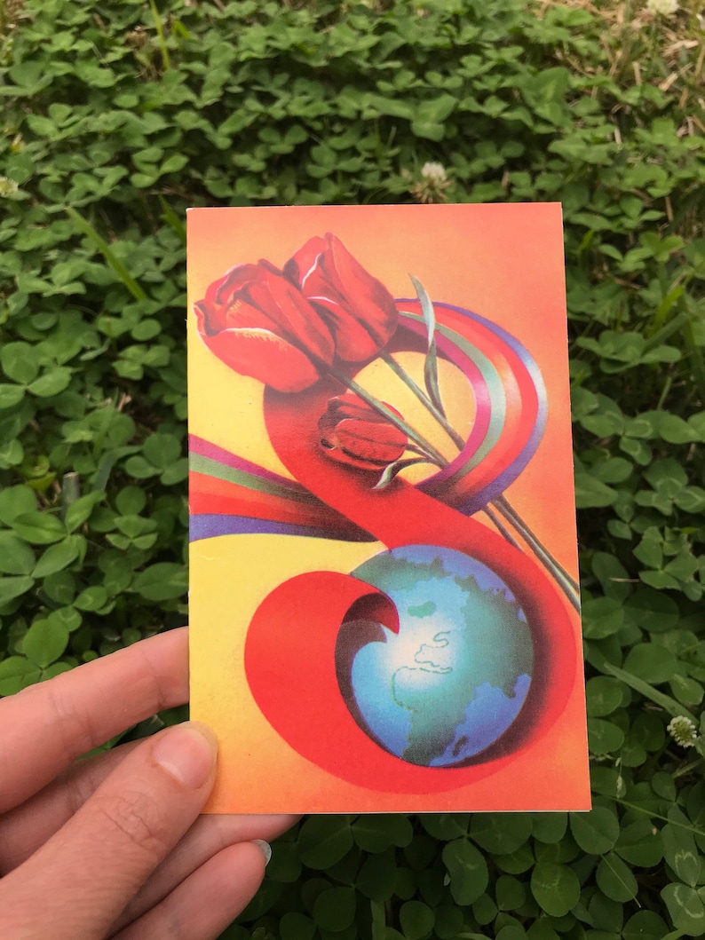 May include: A red, orange, yellow, green, and blue illustration of a globe with three red tulips on top. The globe is surrounded by a rainbow-colored ribbon.