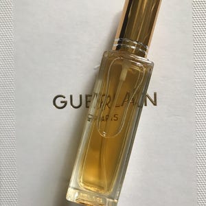 May include: A small, clear glass bottle of perfume with a gold cap and a gold label that reads "Guerlain Paris".