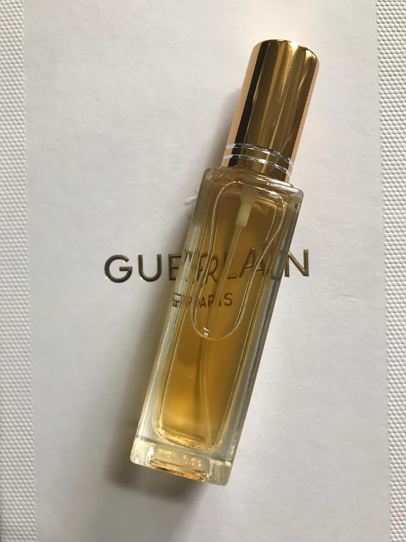 May include: A small, clear glass bottle of perfume with a gold cap and a gold label that reads "Guerlain Paris".