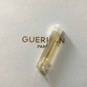 May include: A clear glass vial containing a yellow liquid. The vial has a white cap and is labelled "Guerlain Paris".