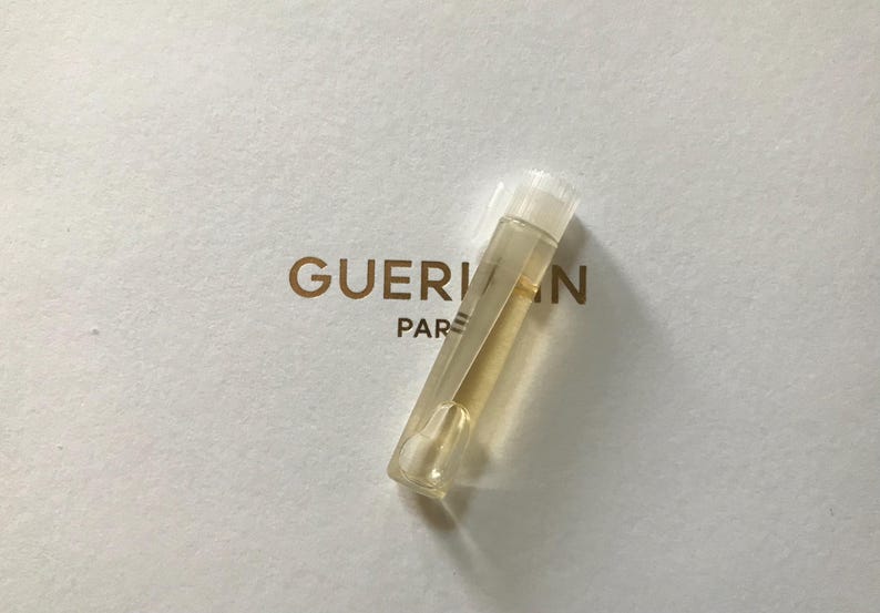 May include: A clear glass vial containing a yellow liquid. The vial has a white cap and is labelled "Guerlain Paris".