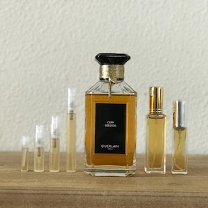 May include: A collection of perfume bottles, including a large bottle of Guerlain Cuir Beluga perfume. The bottles are arranged in a row on a wooden surface.