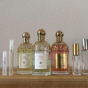 May include: A collection of Guerlain Aqua Allegoria perfumes in various sizes. The bottles have gold-colored honeycomb-patterned tops and labels with the brand name. The fragrances are in clear glass bottles, with some containing a light yellow or pink liquid.