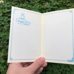 May include: A white card with a blue border and floral design. The card has the text "8 березня" written in blue cursive.