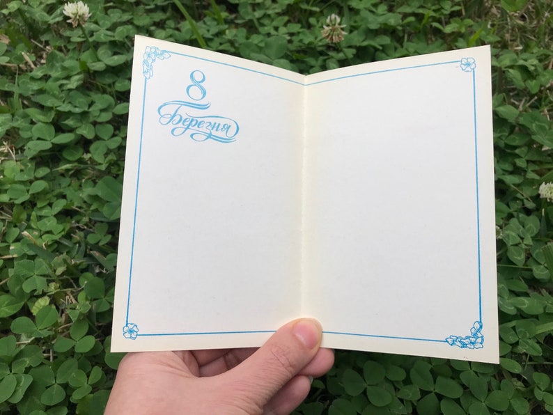 May include: A white card with a blue border and floral design. The card has the text "8 березня" written in blue cursive.