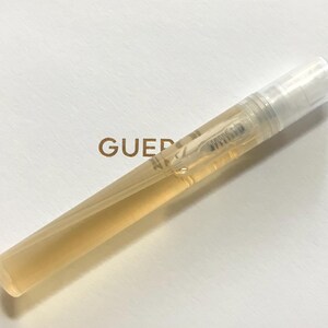 May include: A clear plastic travel-sized bottle of perfume with a gold cap. The bottle is partially filled with a light yellow liquid.
