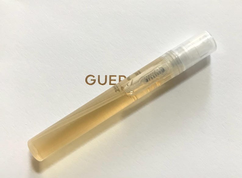 May include: A clear plastic travel-sized bottle of perfume with a gold cap. The bottle is partially filled with a light yellow liquid.